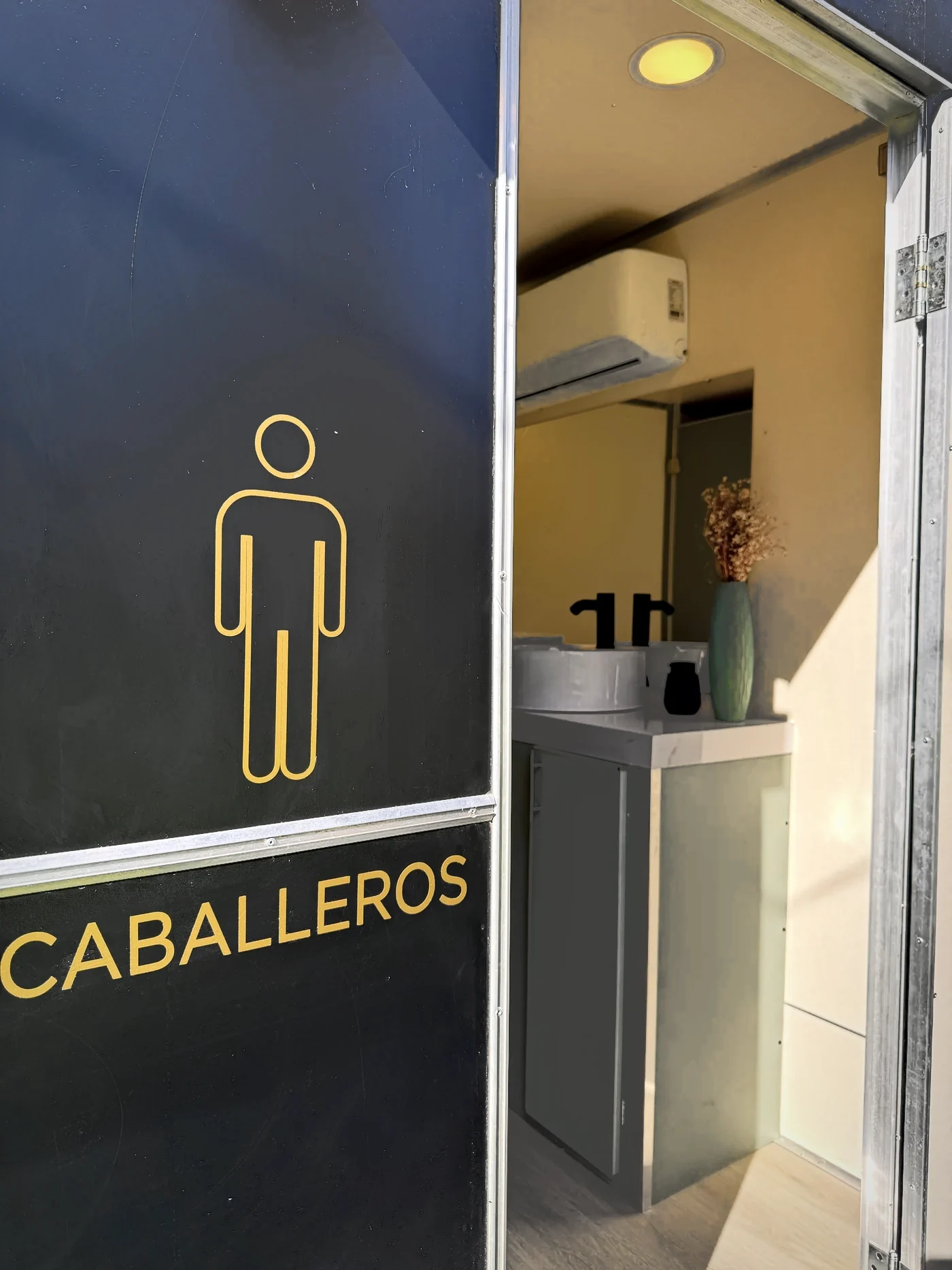 Acceso de caballeros señalizado en dorado sobre el exterior negro.