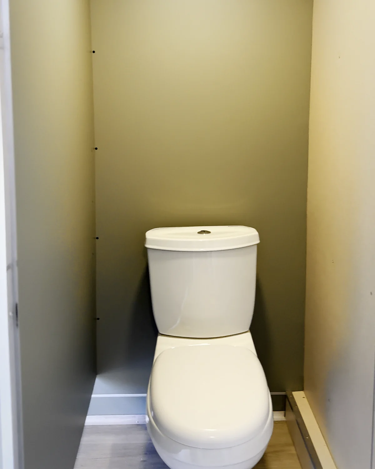 Inodoro dentro de su cubículo cerrado, con piso símil madera.